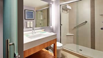Un baño moderno con cabina de ducha de vidrio, un lavamanos blanco con un espejo encima y un inodoro.