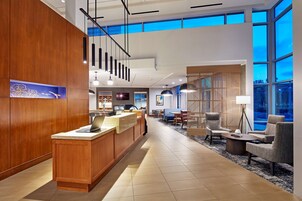Un moderno vestíbulo de hotel con mostrador de recepción, zona de estar y grandes ventanales.