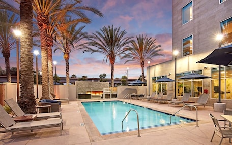 A pool area with lounge chairs, umbrellas, and a fire feature.