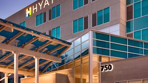 Ein modernes Hotelgebäude mit einem gut sichtbaren 'HYATT PLACE'-Schild, großen Fenstern und einem überdachten Eingangsbereich.