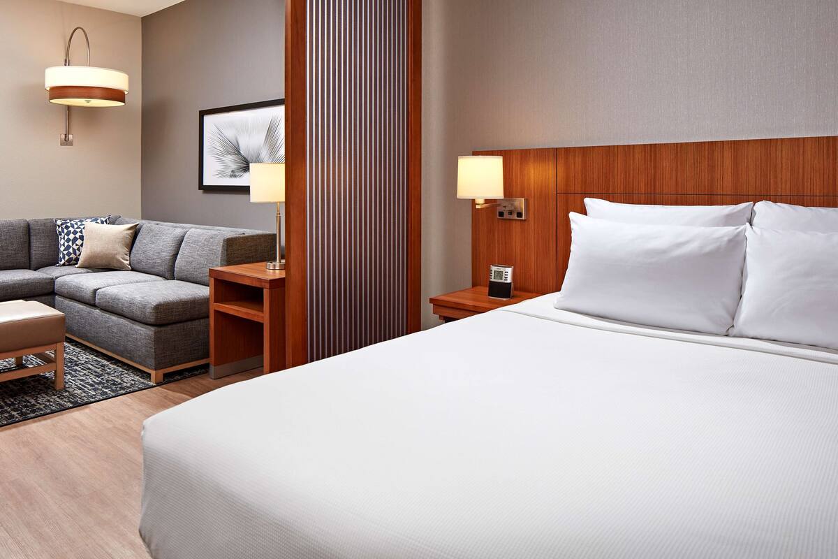 A hotel room with a large bed, a sofa, a side table, a lamp, and a framed picture on the wall.
