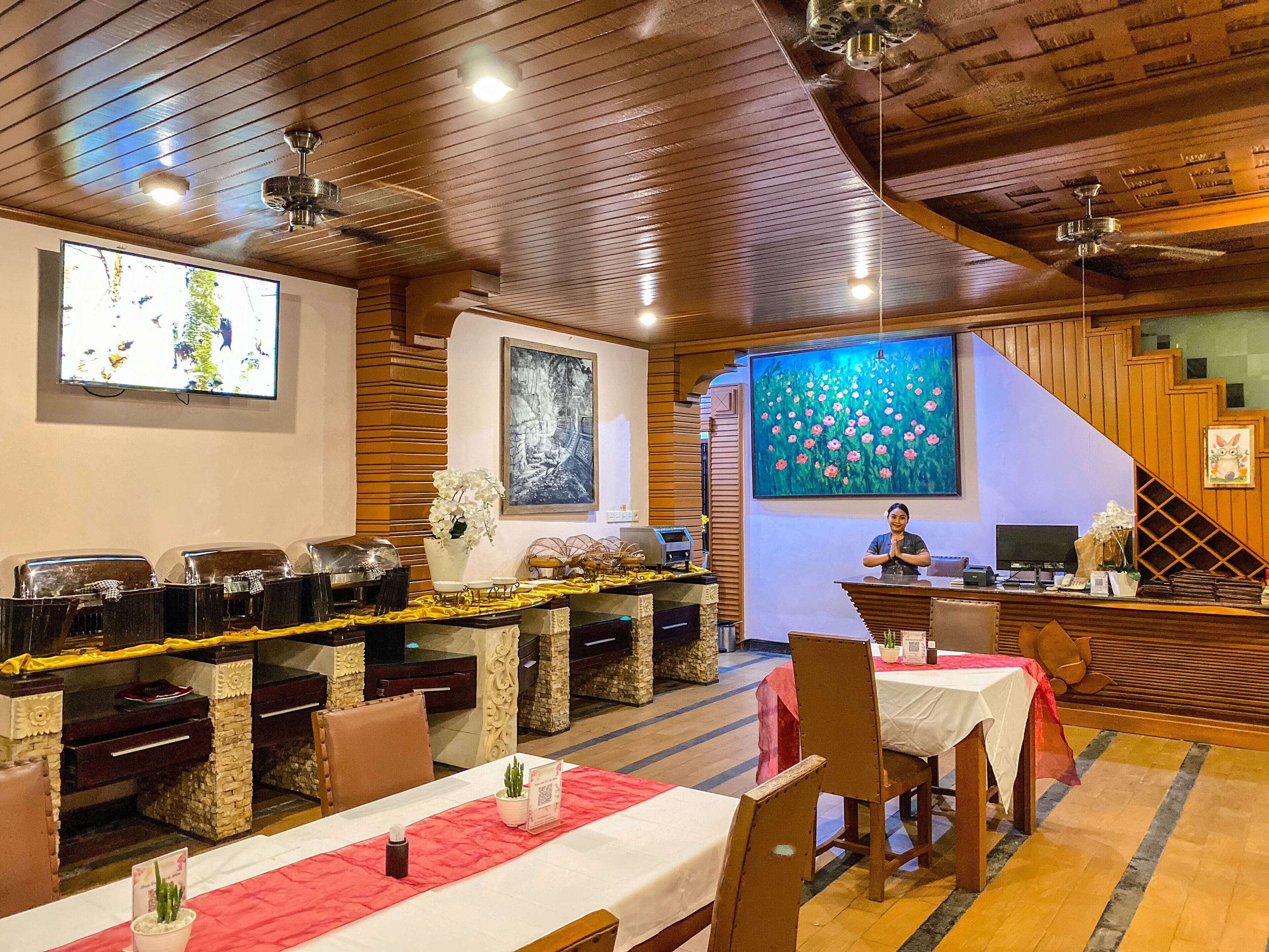 A restaurant with wooden ceiling, a TV screen, and a person at the counter.