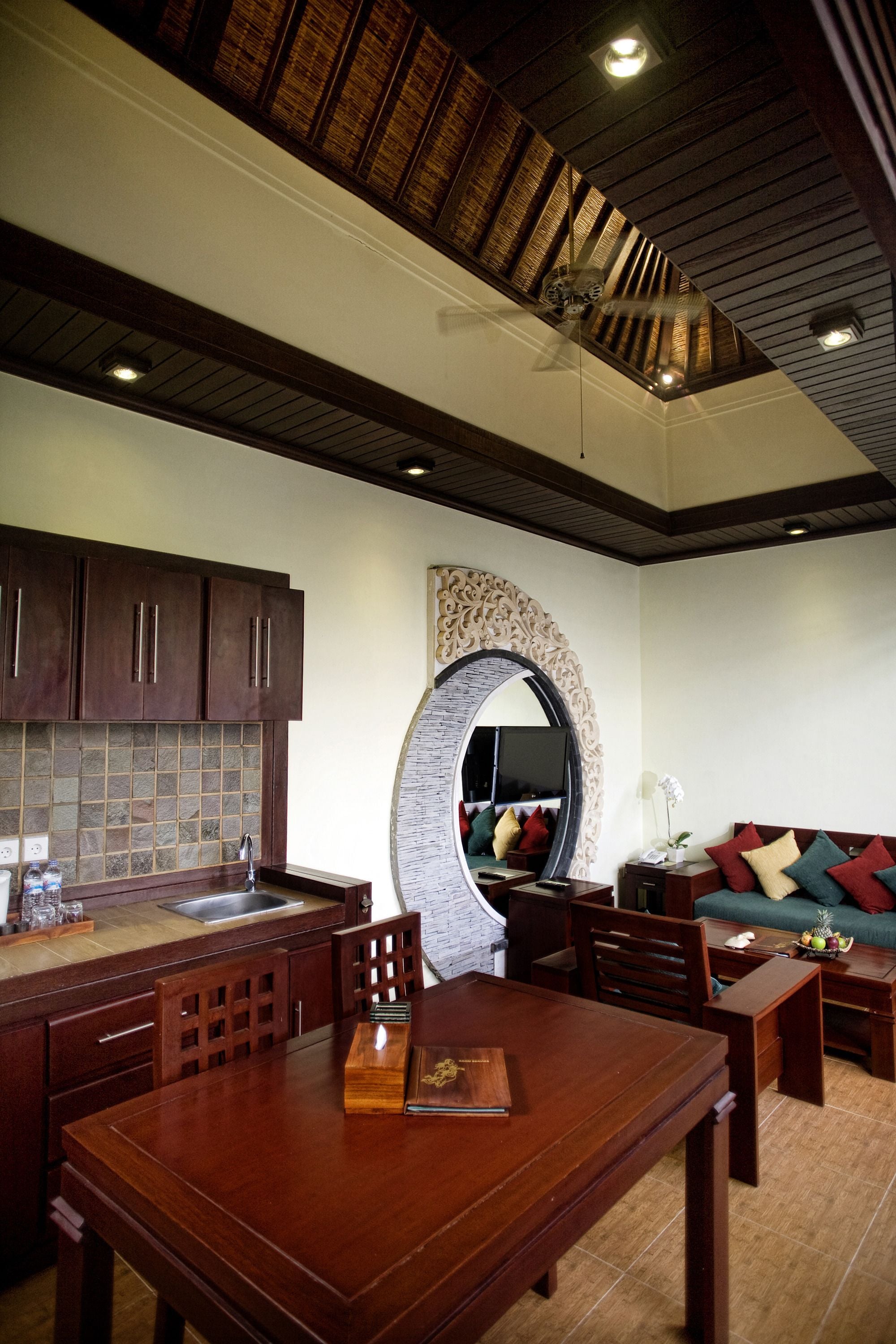 A spacious living area with a wooden dining table, a sofa with cushions, and a large mirror.