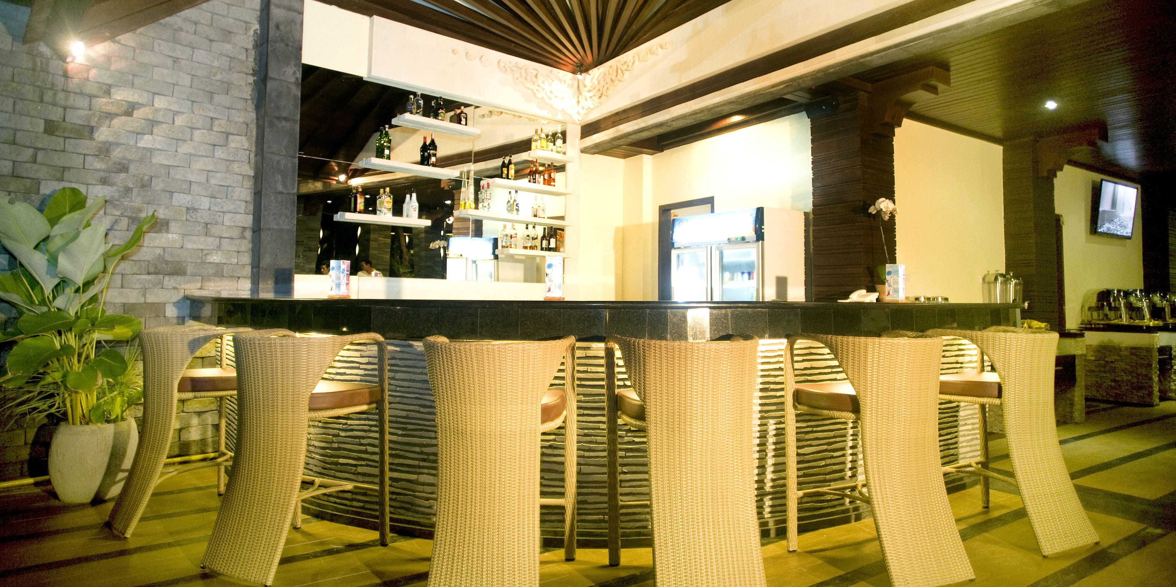A bar area with wicker chairs, a counter with bottles, and a refrigerator.