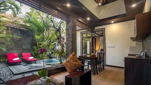 A modern interior with a pool, red lounge chairs, a dining area, and a kitchen. - The Bali Dream Villa Resort Echo Beach Canggu (Pererenan)