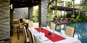 A restaurant with a pool view, featuring a stone wall, wooden furniture, and a red table runner. - The Bali Dream Villa Resort Echo Beach Canggu (Pererenan)