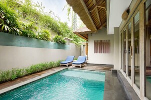 Uma área de piscina com duas espreguiçadeiras, um telhado de palha e vegetação exuberante.