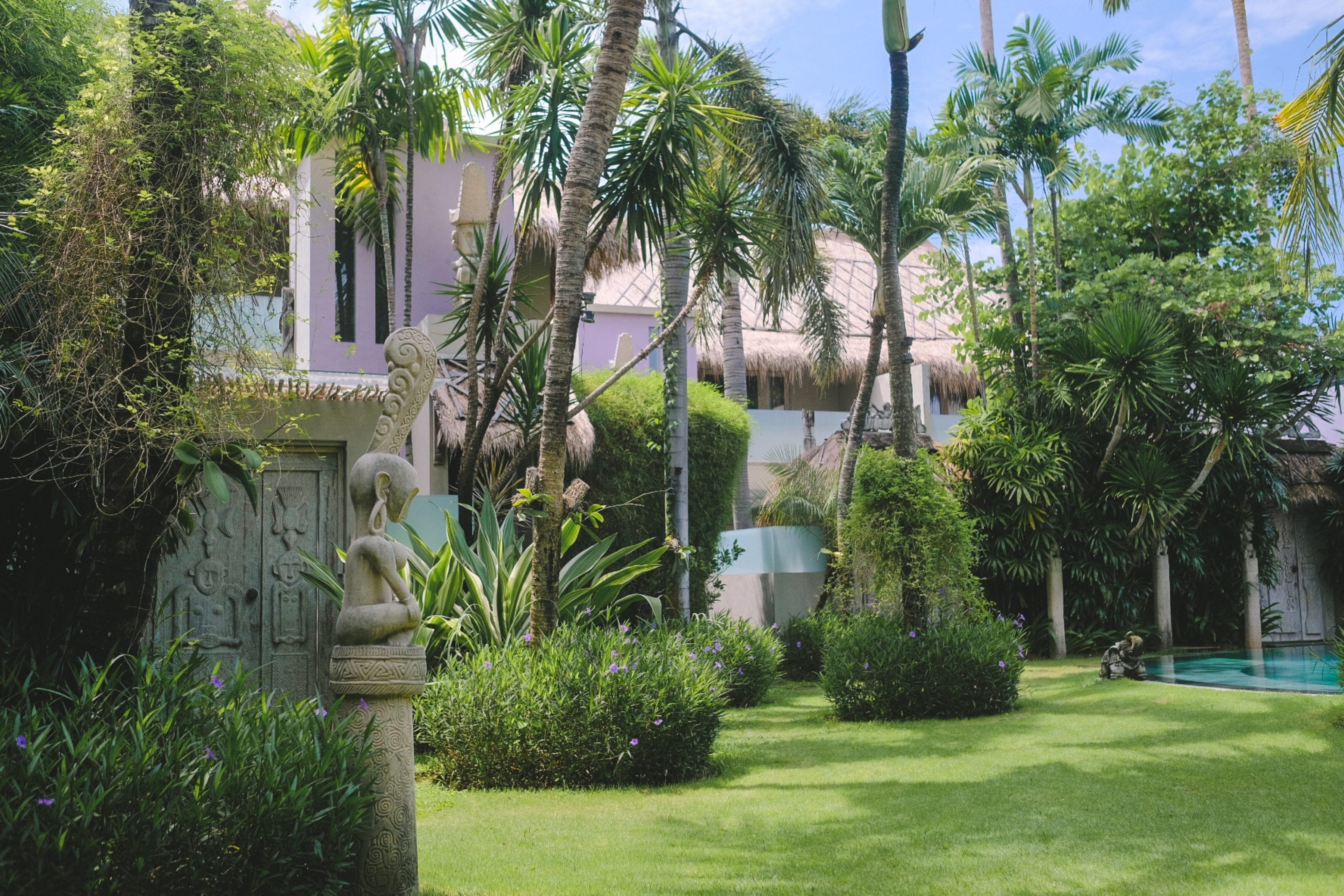 Un jardin luxuriant agrémenté d’une statue, d’une piscine et d’un bâtiment au toit de chaume.