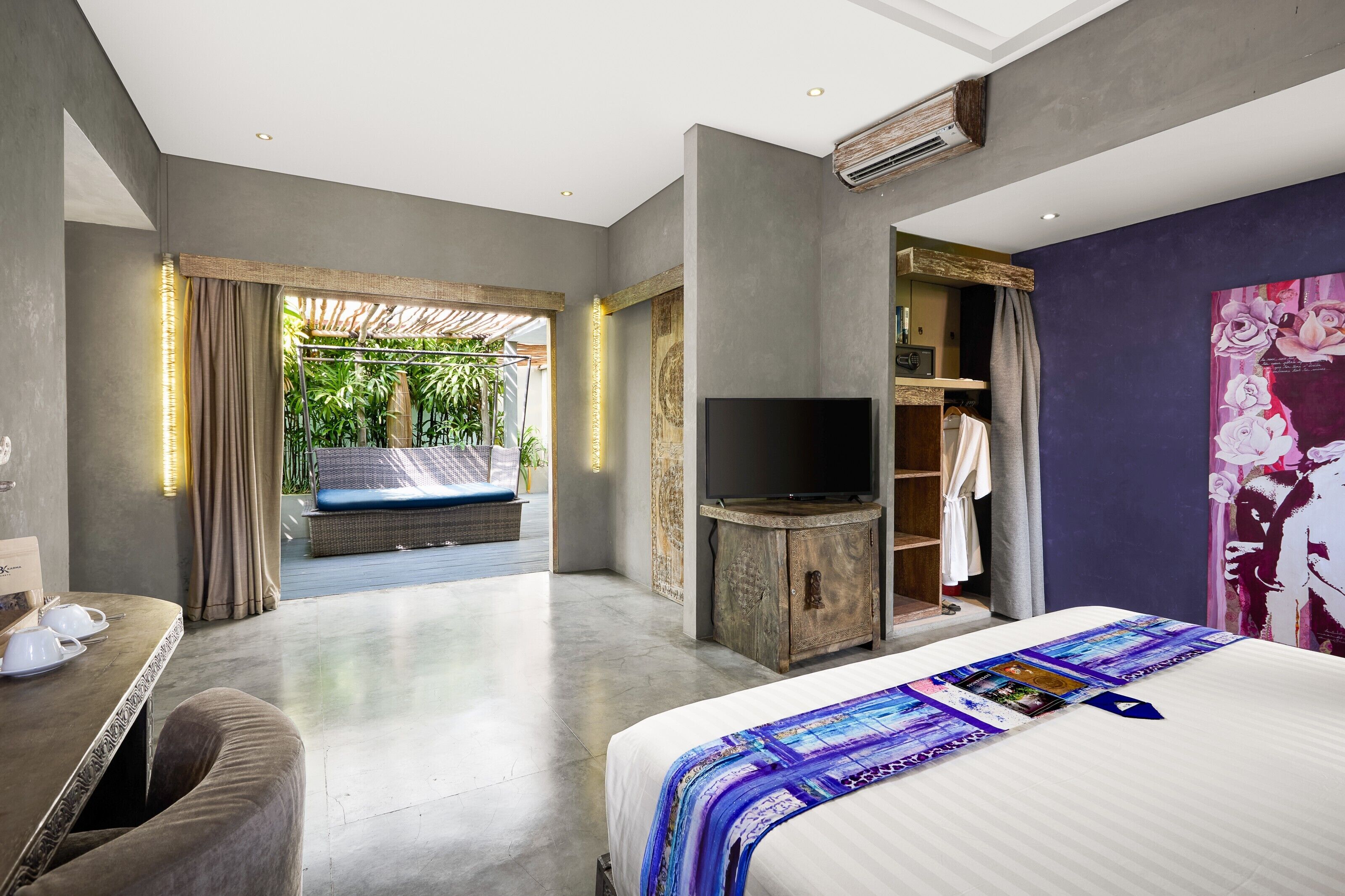 A modern hotel room with a large bed, a television, a seating area with a view of greenery, and a wardrobe.