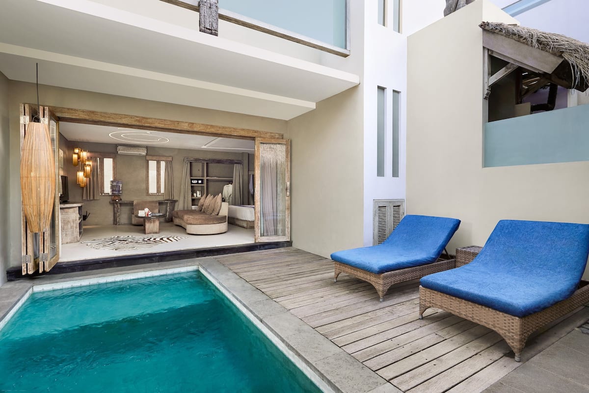 A poolside area with wicker lounge chairs, a pool, and a view into a well-furnished interior space.