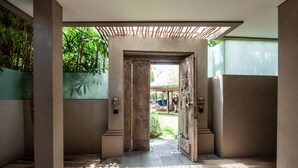 An interior corridor with a wooden floor, a large open door leading outside, and a view of a garden area. - Blue Karma Dijiwa Seminyak (Seminyak)