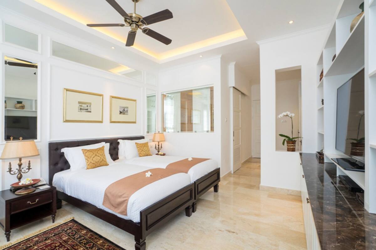 Une chambre spacieuse avec un grand lit, des tables de chevet, un ventilateur de plafond et un téléviseur.