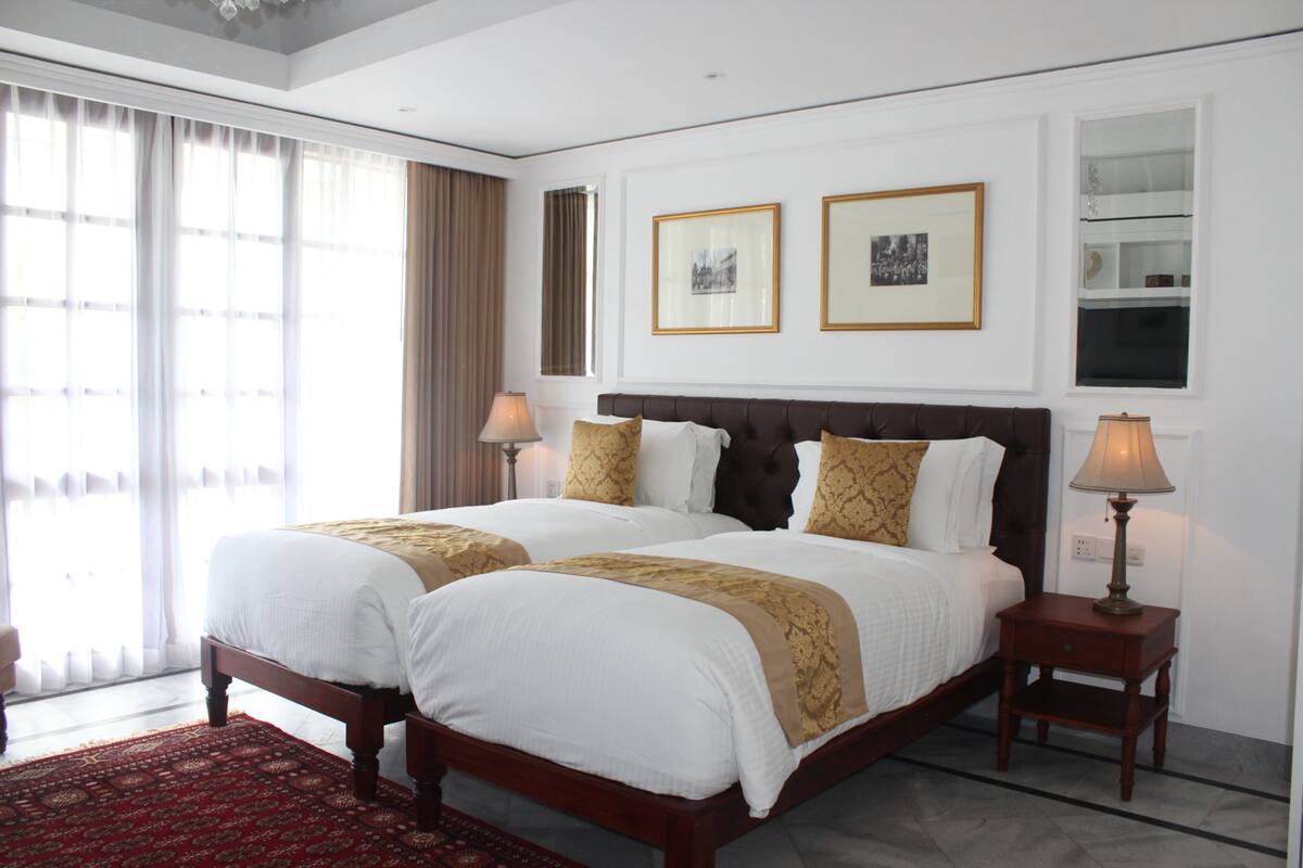 Une chambre d’hôtel avec deux lits, un tapis rouge à motifs et une grande fenêtre avec des rideaux.