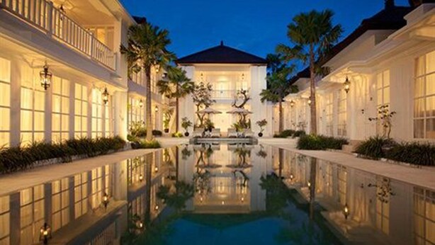 Un hôtel de luxe doté d’un bassin central reflétant la lumière, d’une architecture élégante et de jardins bien entretenus.