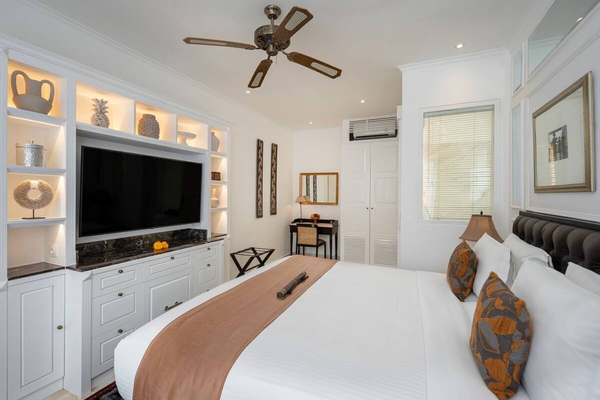 Une chambre d’hôtel avec un grand lit, une télévision, un bureau et un ventilateur de plafond.