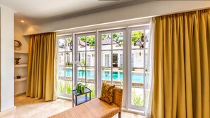 A room with a pool view, a sofa, a table, and curtains. - The Colony Hotel (Seminyak)