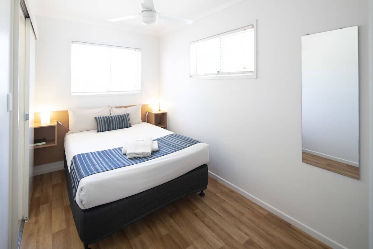 Une chambre à coucher avec un lit, des tables de chevet, un ventilateur de plafond et des fenêtres.