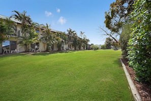 A well-maintained grassy courtyard with a wooden fence, surrounded by buildings with balconies and outdoor seating.