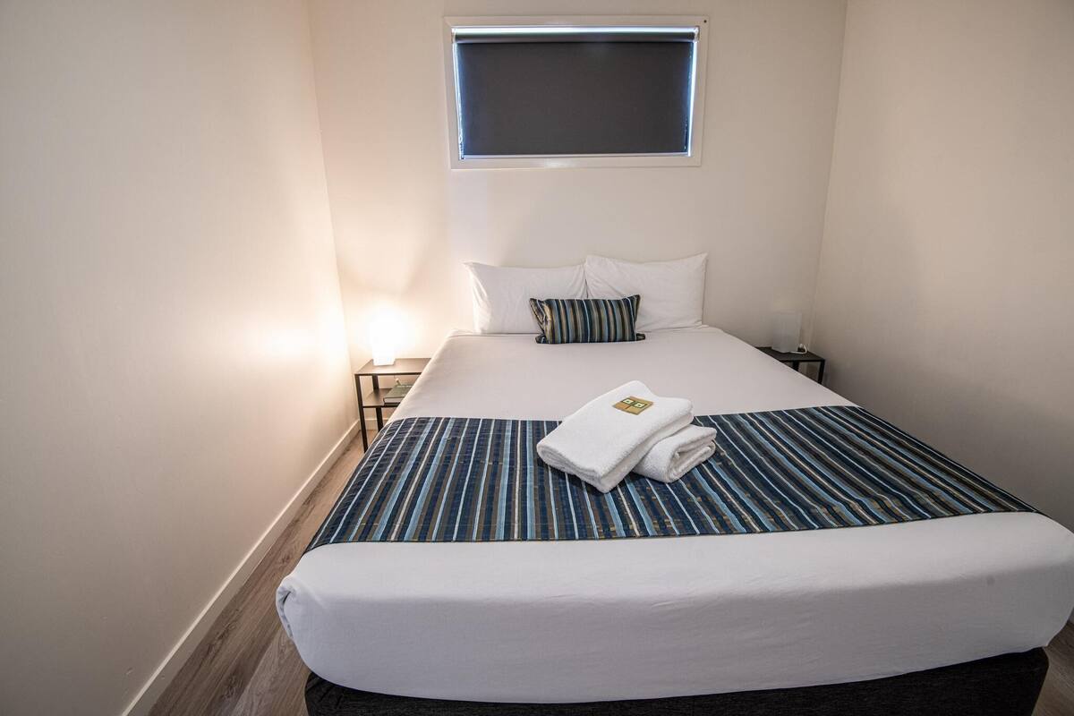 Une chambre d’hôtel avec un lit, une fenêtre, une table de chevet et une lampe.