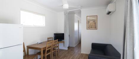 Una habitación compacta con una mesa de comedor de madera, un sofá negro, un ventilador de techo, un televisor y un cuadro en la pared.