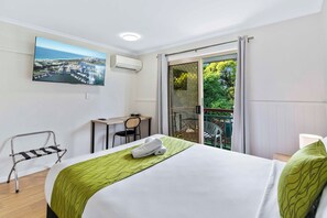 Une chambre d’hôtel comprenant un lit, un bureau, une chaise, un balcon avec vue sur la verdure et un appareil de climatisation.