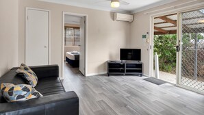 Un salon moderne avec un canapé en cuir noir, un téléviseur posé sur un meuble noir et un ventilateur de plafond.