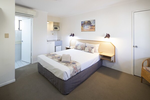 A hotel room with a bed, bedside table, lamp, and a painting on the wall.