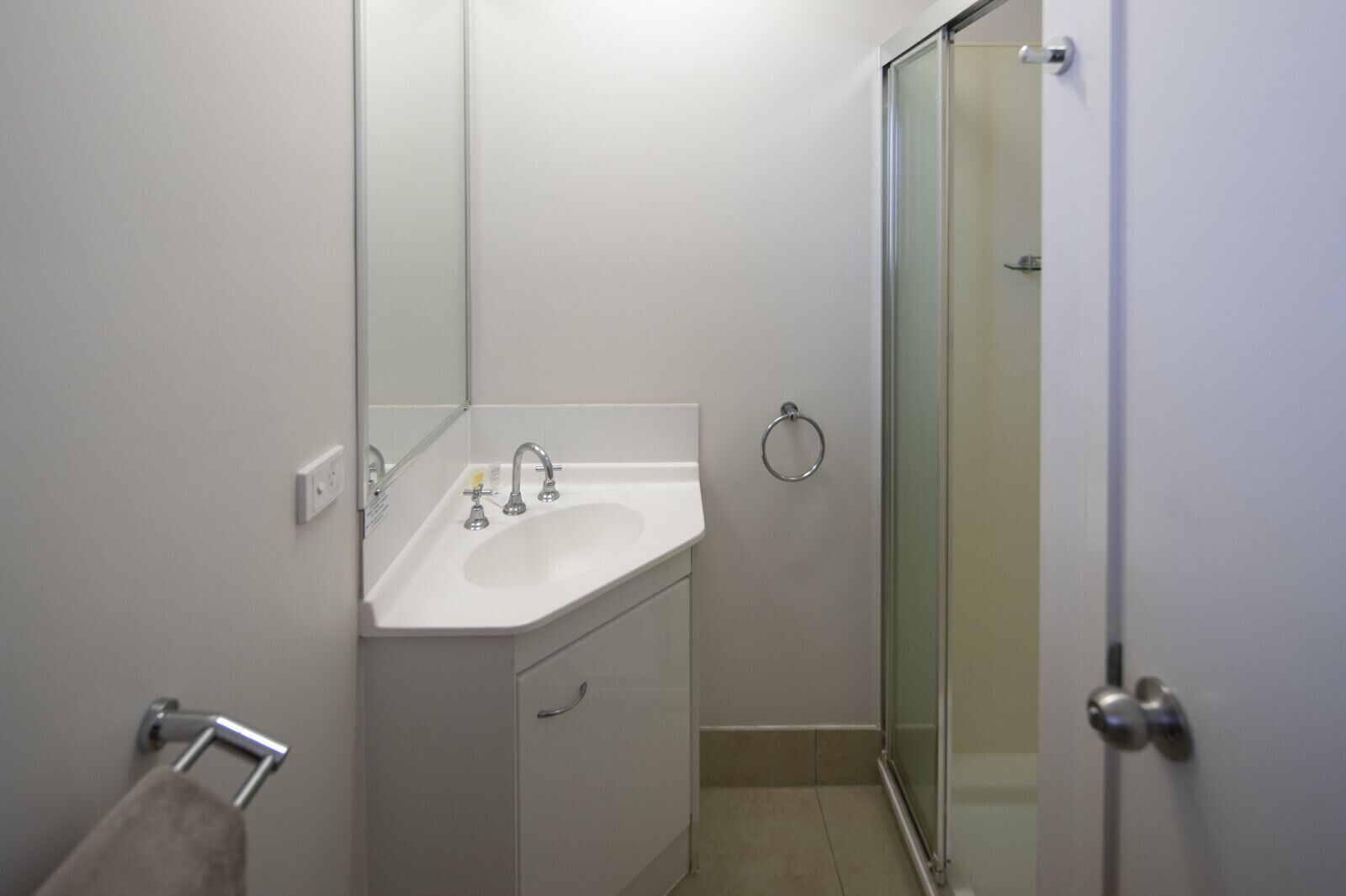 A bathroom with a white sink, two faucets, a mirror, a towel rack, and a glass shower door.