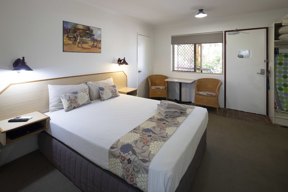 Une chambre d’hôtel avec un grand lit, un bureau, deux chaises, un tableau au mur et une fenêtre.
