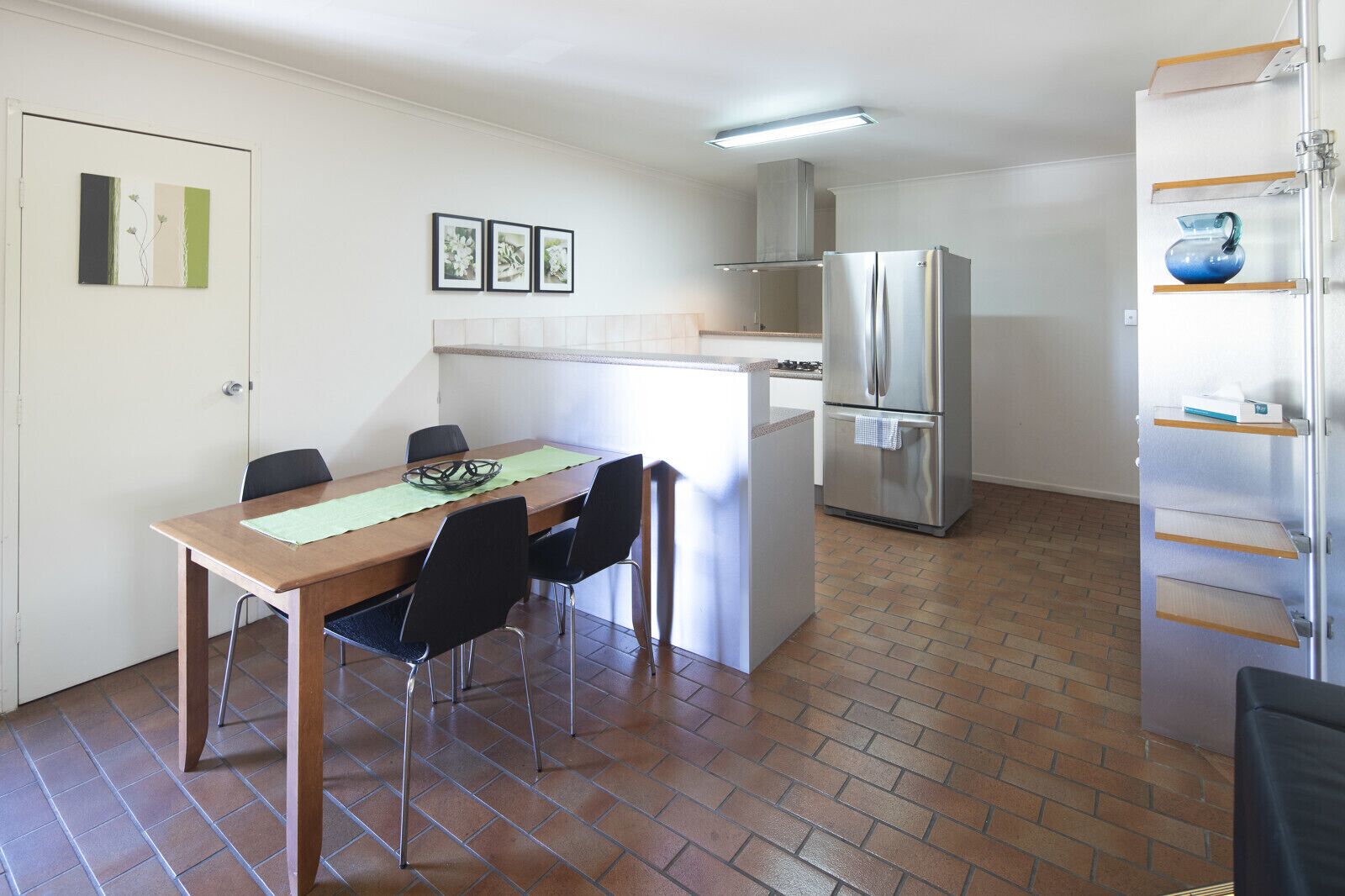 Cocina compacta con comedor, que incluye un refrigerador de acero inoxidable, una pequeña isla con pileta y piso de cerámica.
