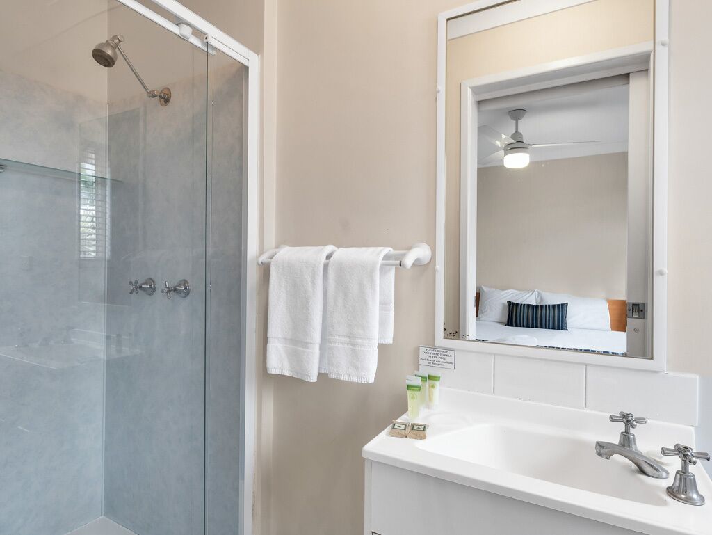 Un baño con cabina de ducha de vidrio, un lavabo blanco con dos grifos y un espejo sobre el lavabo.