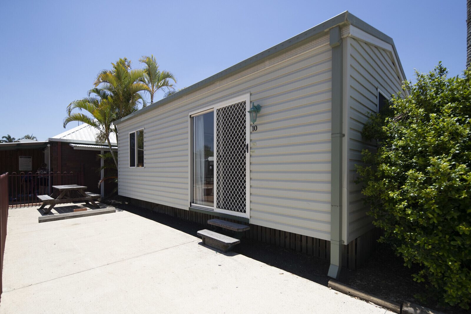 A mobile home with a fenced patio area, a small table, and a bench.