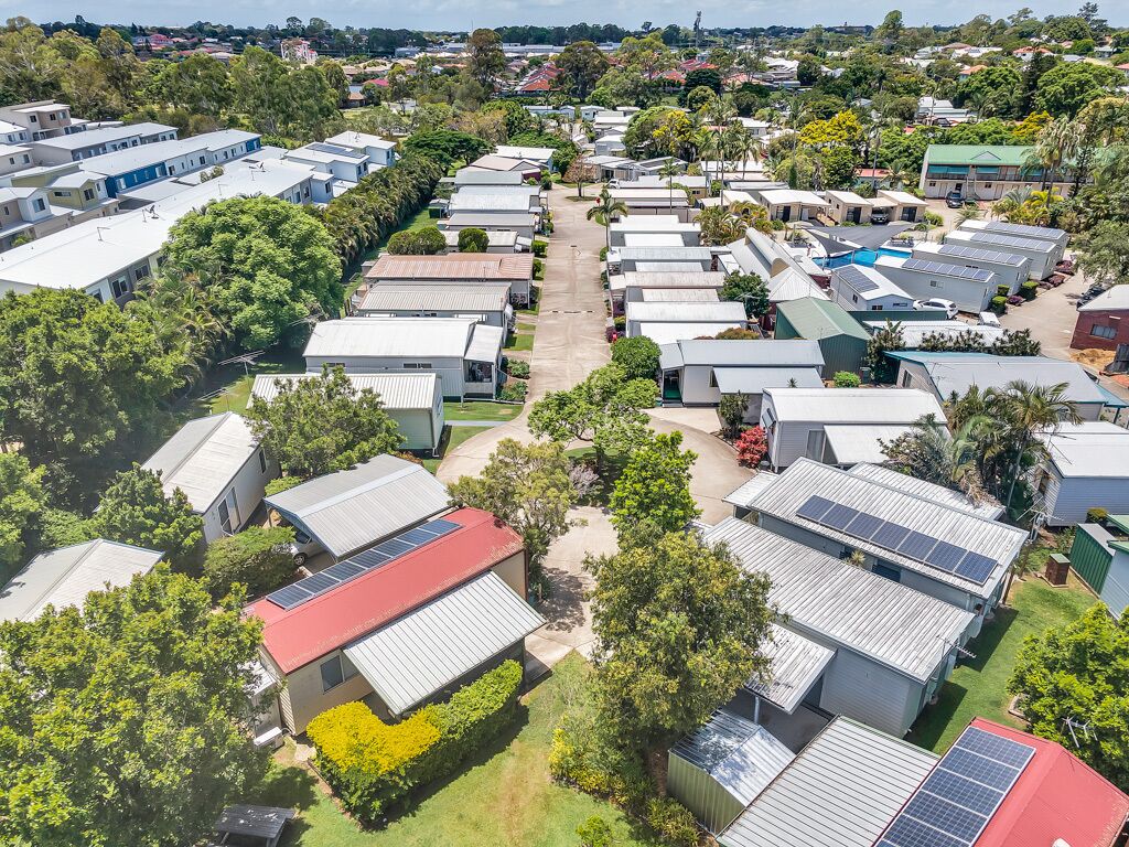 A residential area with multiple single-story houses, some with solar panels, surrounded by greenery and trees.