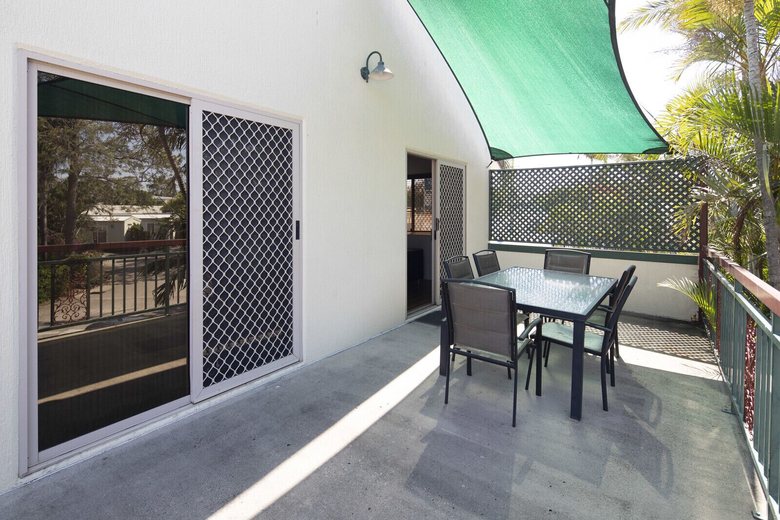 Un balcon avec une table et des chaises, un parasol vert et un treillis.