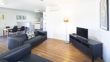 Ein modernes Wohnzimmer mit einer Couch, einem Fernseher und einem Essbereich mit Stühlen und einem Tisch.