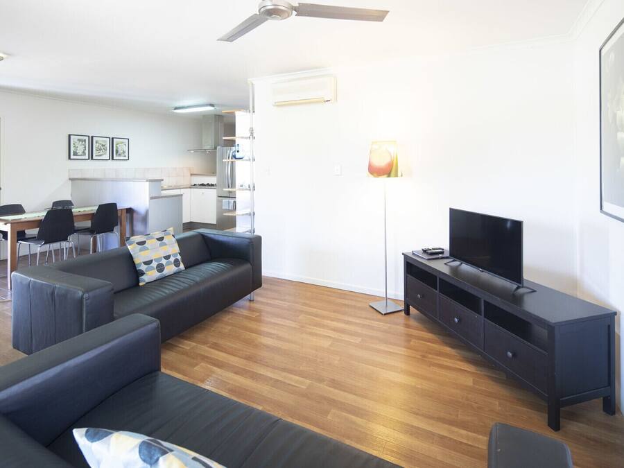 Ein modernes Wohnzimmer mit einer Couch, einem Fernseher und einem Essbereich mit Stühlen und einem Tisch.