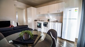Une cuisine moderne avec des meubles blancs, un four encastré, un four à micro-ondes et un réfrigérateur. On y trouve une table à manger avec des chaises et une plante en pot.