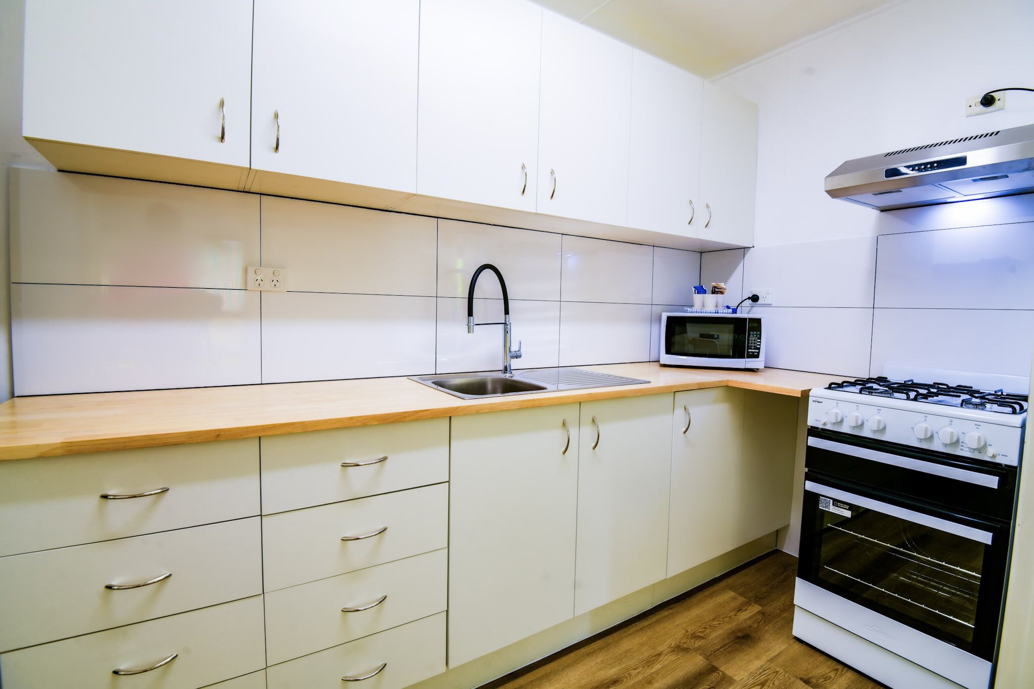 Una cocina moderna con armarios blancos, un lavamanos de acero inoxidable, un microondas y una estufa a gas.