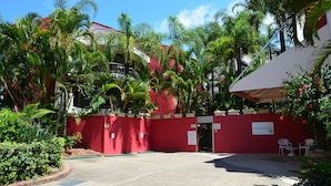 Een toegangshek met een rode muur, palmbomen en een bord met 'Enderley Gardens'.