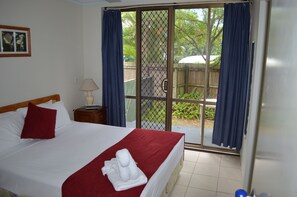 A hotel room with a bed, a nightstand, a lamp, and a view through a sliding glass door to an outdoor area with greenery. - Enderley Gardens Resort (Surfers Paradise)
