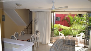 Een woonkamer met een bank, eettafel, stoelen en een balkon met planten.