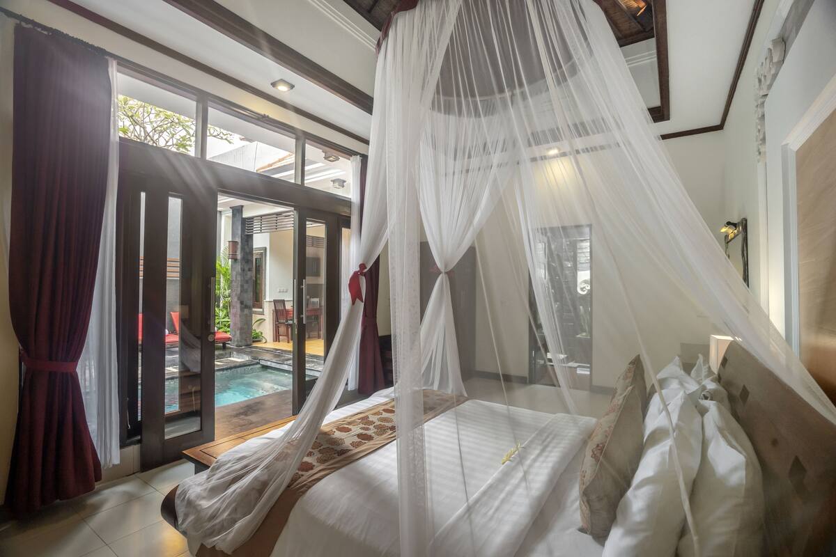 A bedroom with a canopy bed, a view of a swimming pool, and a sliding glass door leading to an outdoor area.