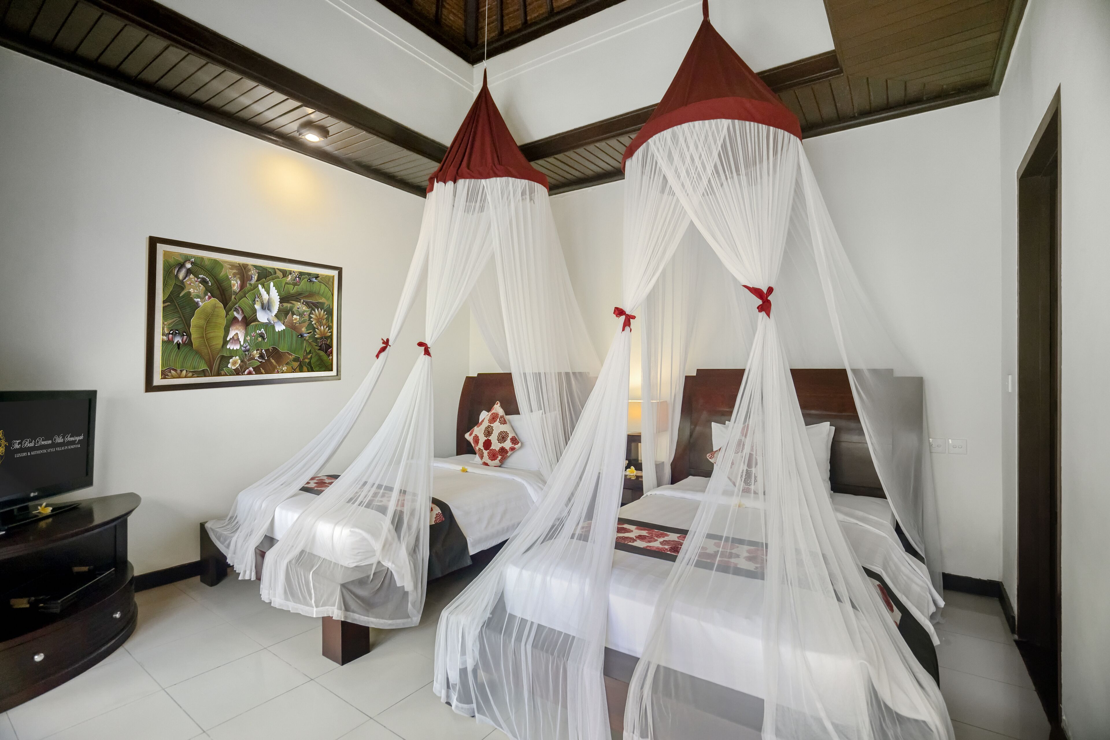A hotel room with a bed under a canopy, a television, and a painting on the wall.
