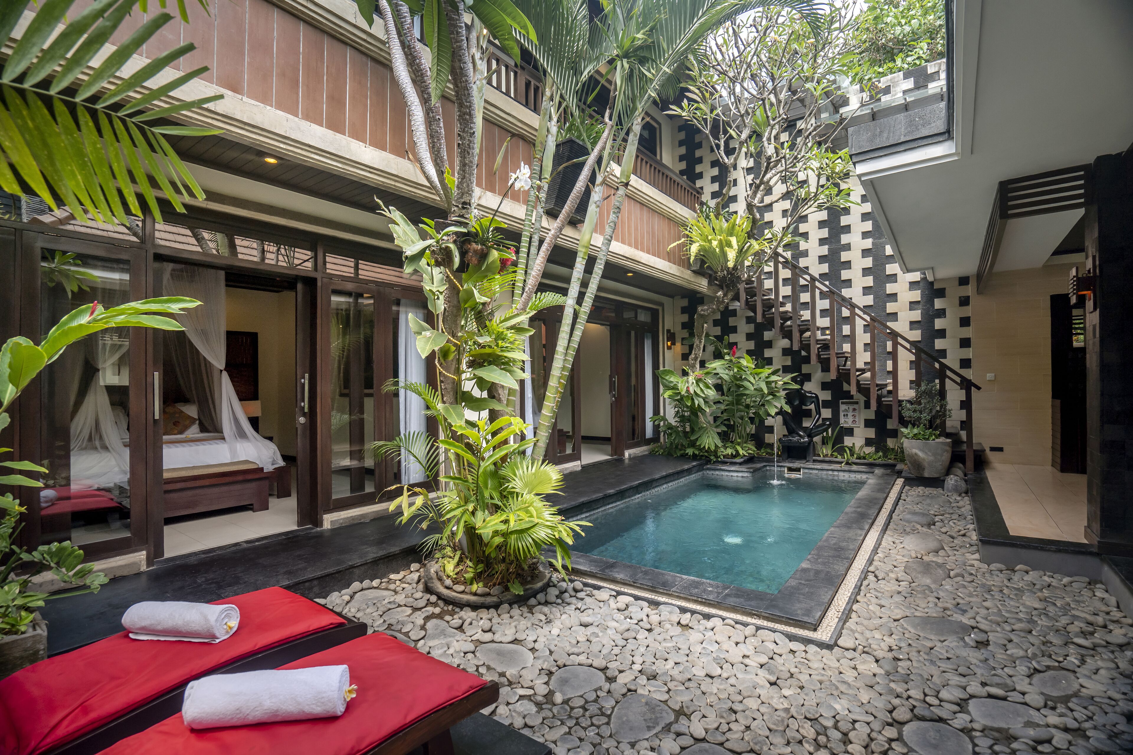 A spa area with a pool, red lounge chairs, and a staircase leading to a balcony.