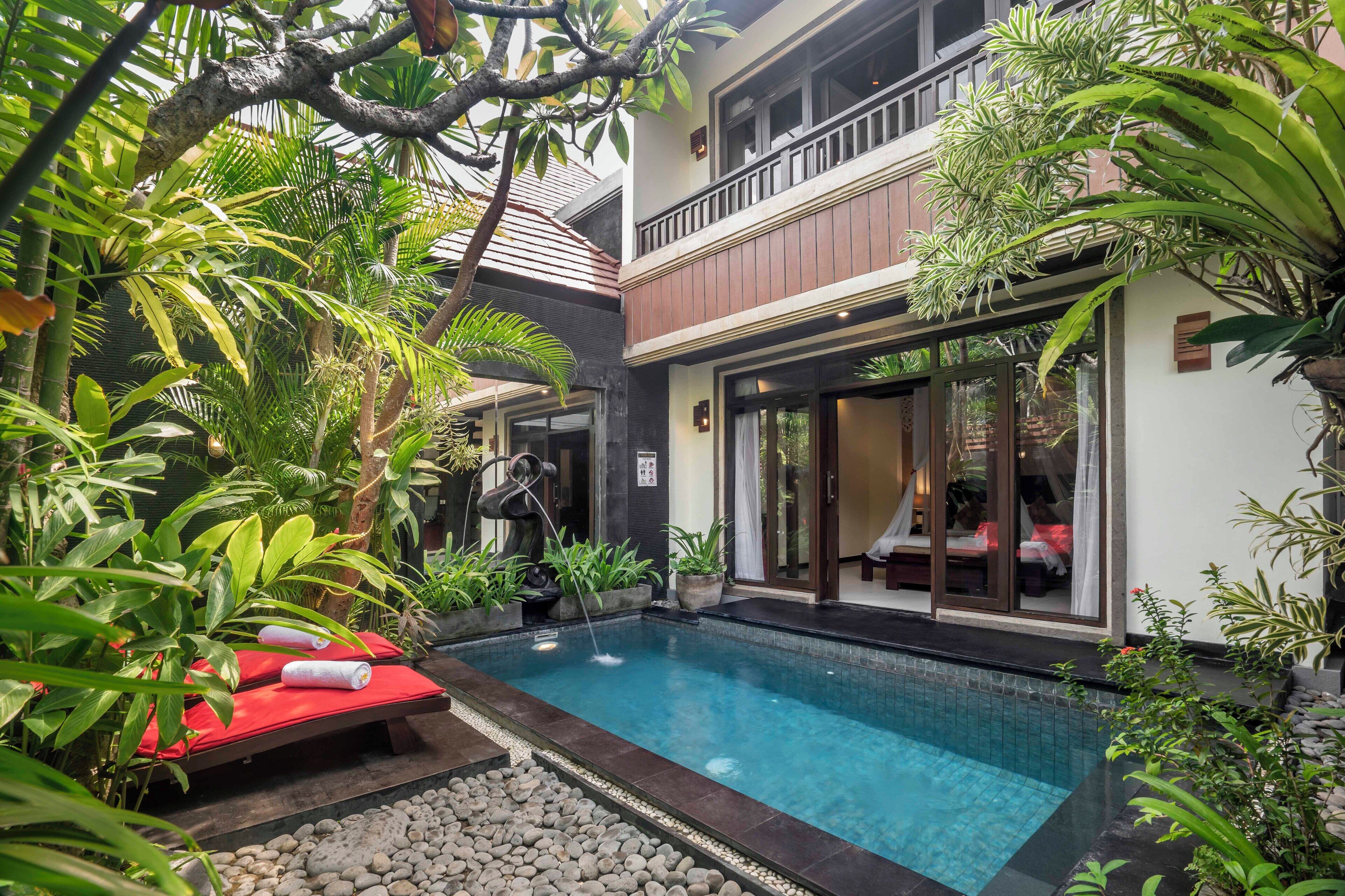 A pool area with a red lounge chair, a small waterfall feature, and lush greenery.