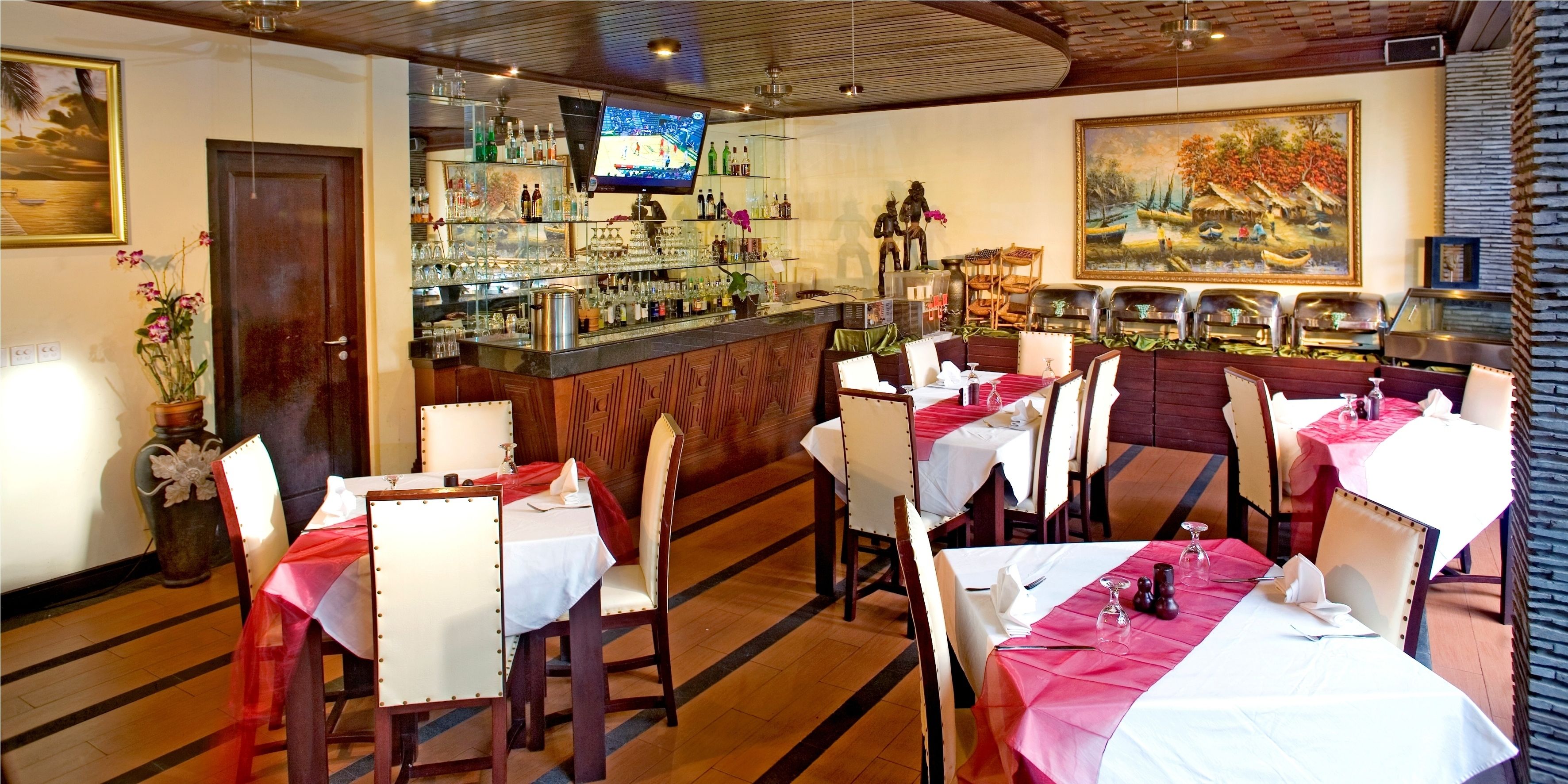 A restaurant with multiple tables, chairs, a bar area, and a television screen.