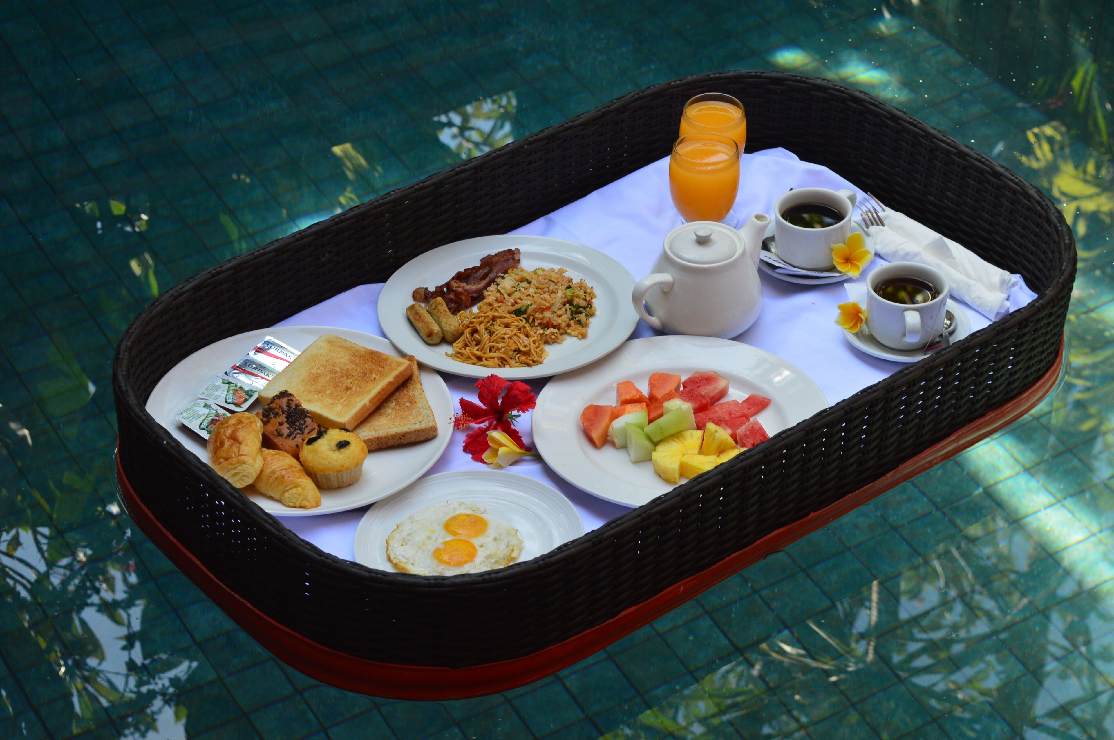 A breakfast tray with toast, eggs, bacon, and fruit by a pool.