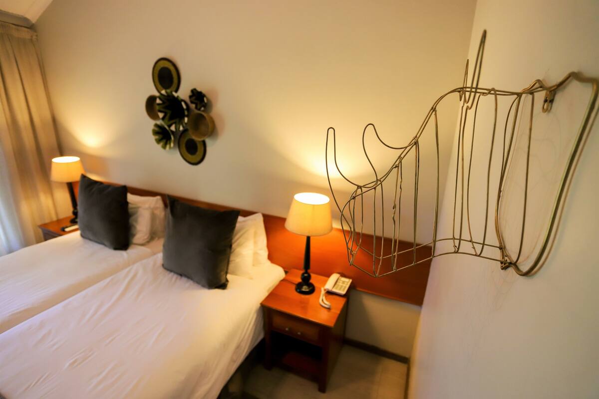 Habitación de hotel con cama doble, dos mesitas de noche, una lámpara, teléfono y un adorno en la pared.