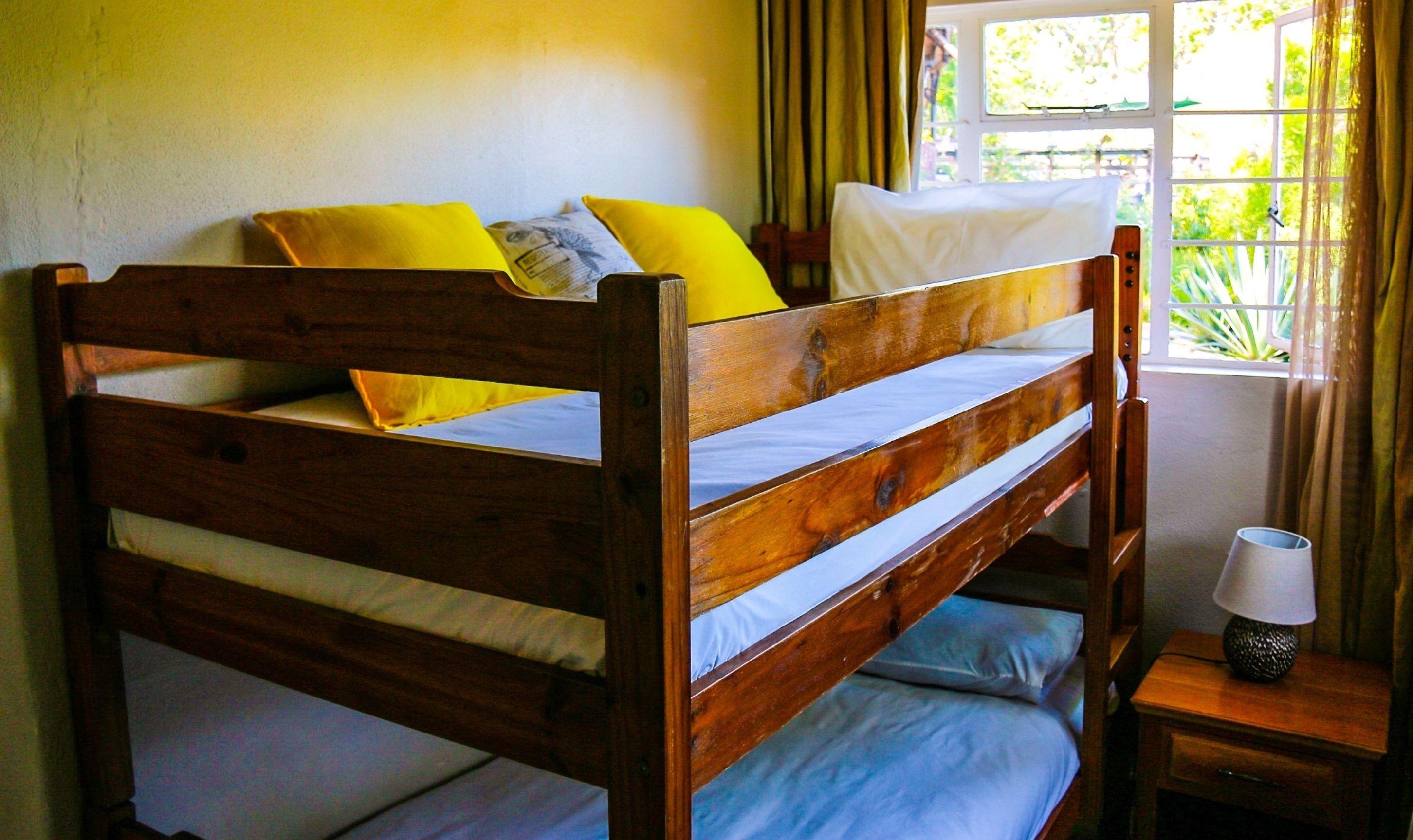 A wooden bunk bed with two pillows, a bedside lamp, and a window with curtains.