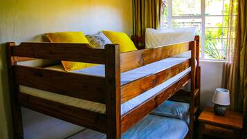 A wooden bunk bed with two pillows, a bedside lamp, and a window with curtains.